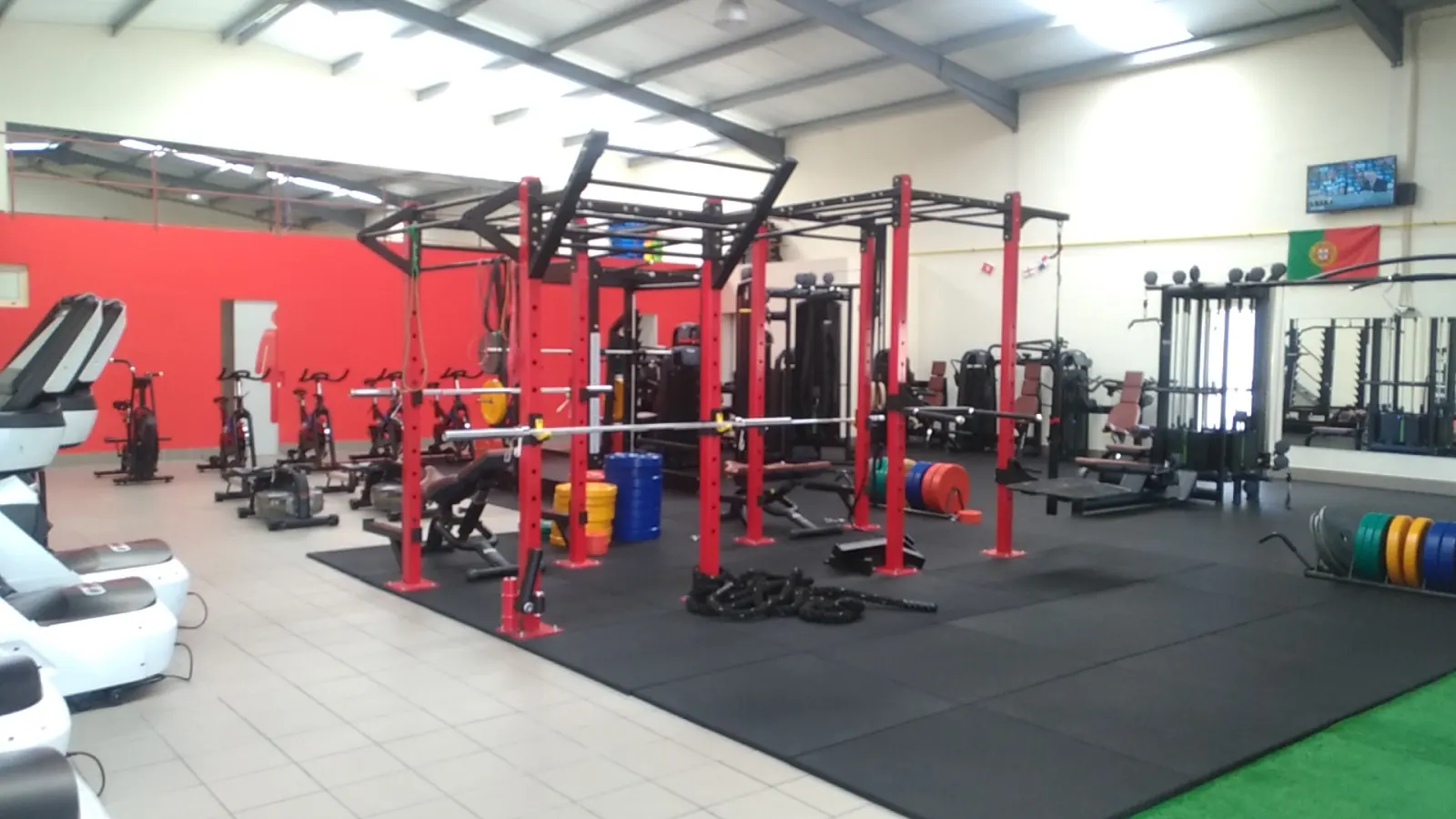Sala de musculação do Fit Arena, com racks vermelhos, pesos e piso de borracha preto